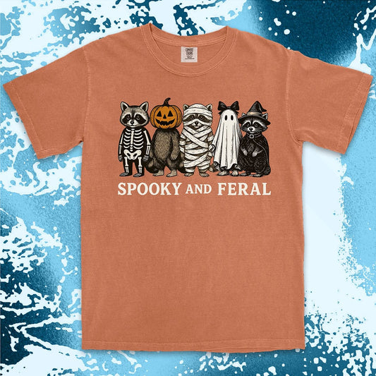 Comfort Color t-shirt with five raccoons in Halloween costumes (skeleton, pumpkin, mummy, ghost, witch) and text “Spooky and Feral.”
