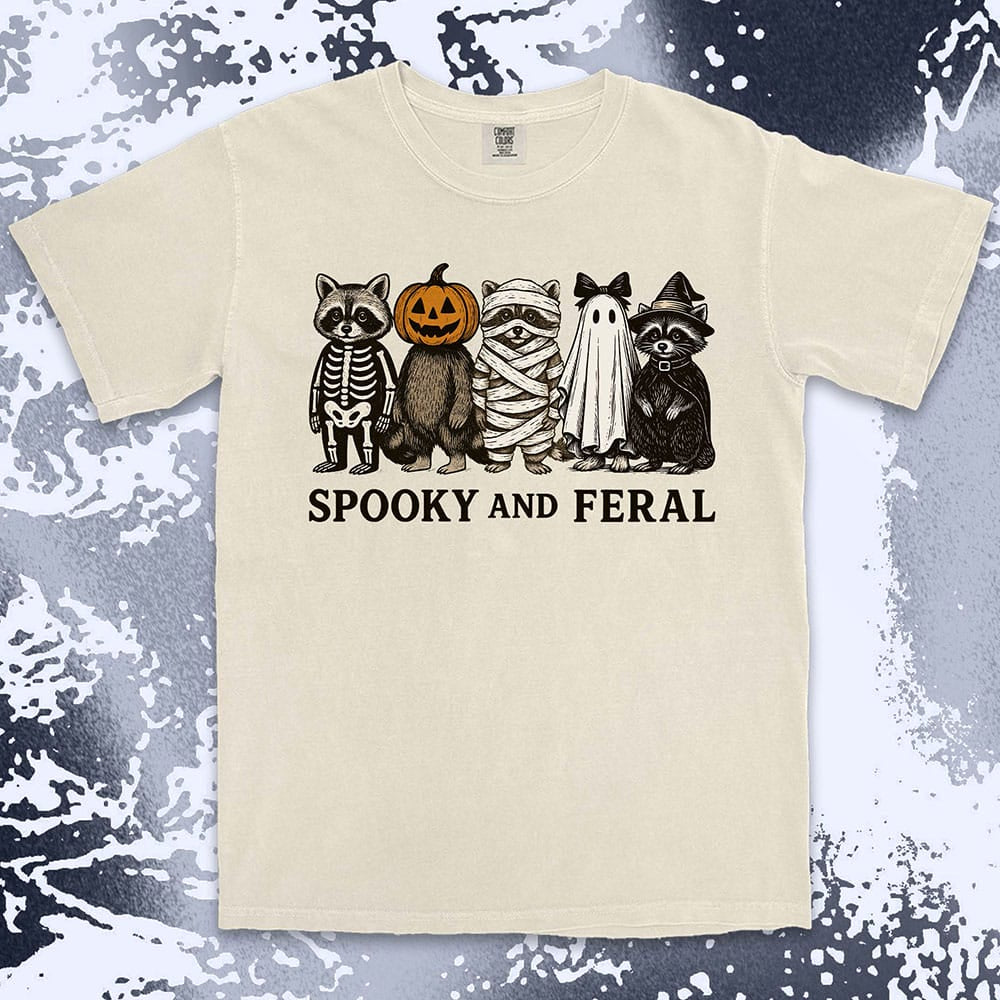 Comfort Color t-shirt with five raccoons in Halloween costumes (skeleton, pumpkin, mummy, ghost, witch) and text “Spooky and Feral.”