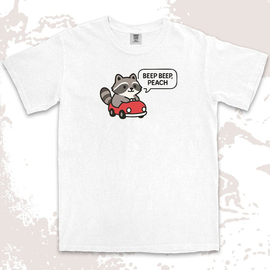 Comfort Color t-shirt with cute chibi raccoon driving a red car and speech bubble saying “Beep beep, peach.”