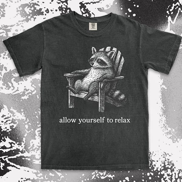 Comfort Color t-shirt with raccoon lounging on a chair and text “Allow yourself to relax” in a calm design.