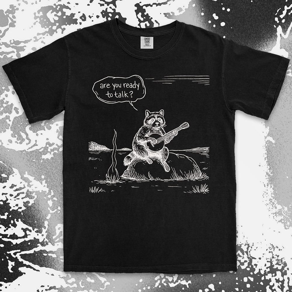 Comfort Color t-shirt with raccoon playing banjo by campfire and speech bubble saying “Are you ready to talk?”