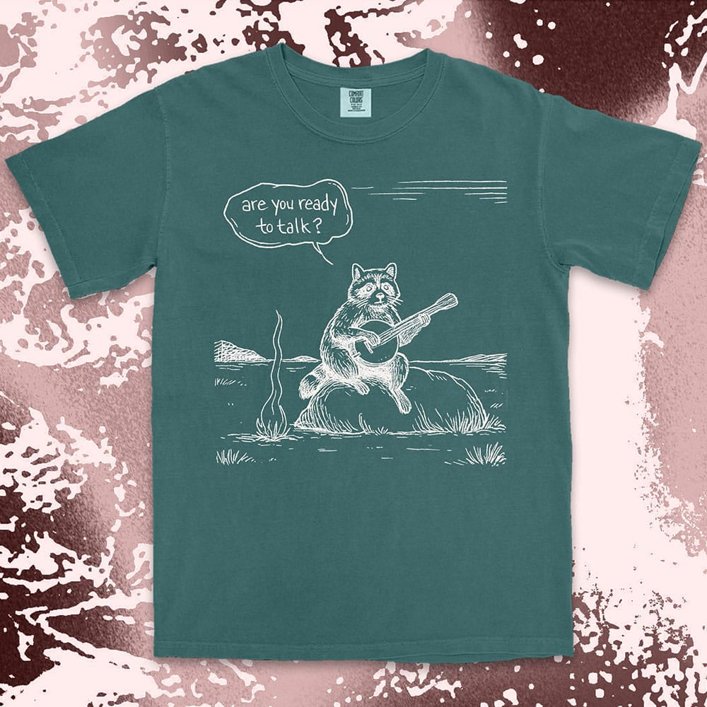 Comfort Color t-shirt with raccoon playing banjo by campfire and speech bubble saying “Are you ready to talk?”