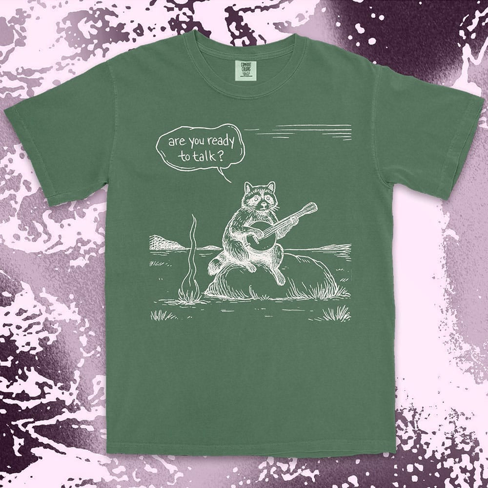 Comfort Color t-shirt with raccoon playing banjo by campfire and speech bubble saying “Are you ready to talk?”