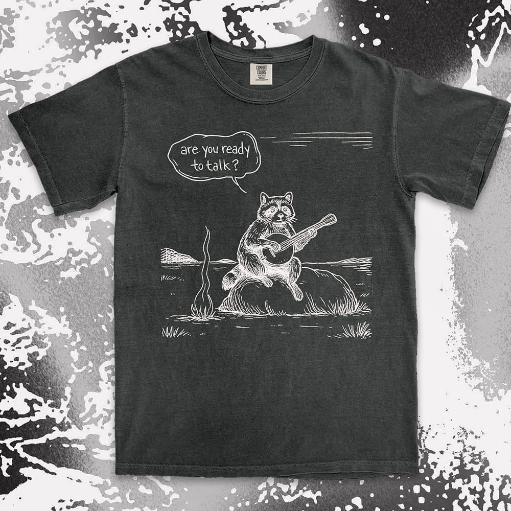 Comfort Color t-shirt with raccoon playing banjo by campfire and speech bubble saying “Are you ready to talk?”