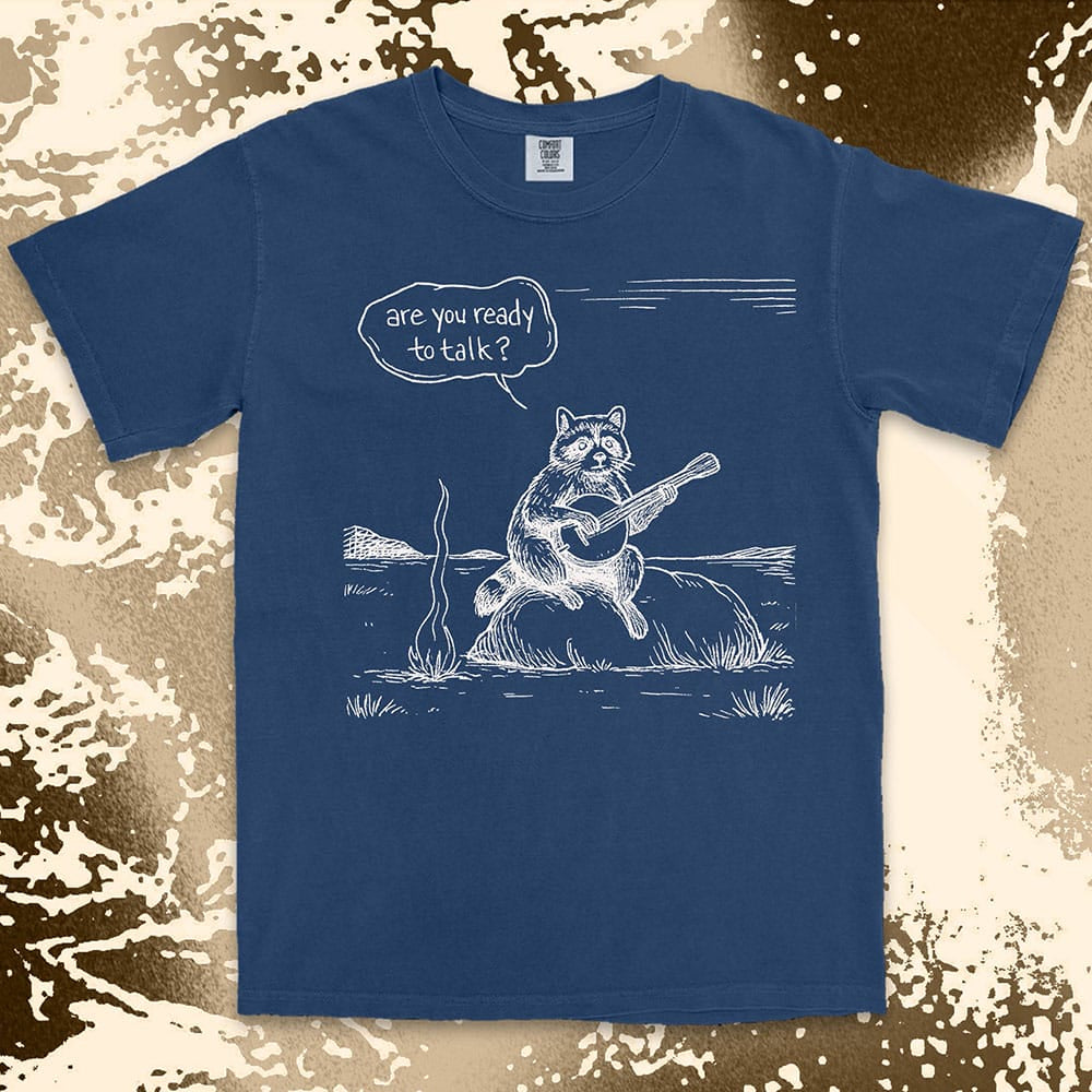 Comfort Color t-shirt with raccoon playing banjo by campfire and speech bubble saying “Are you ready to talk?”