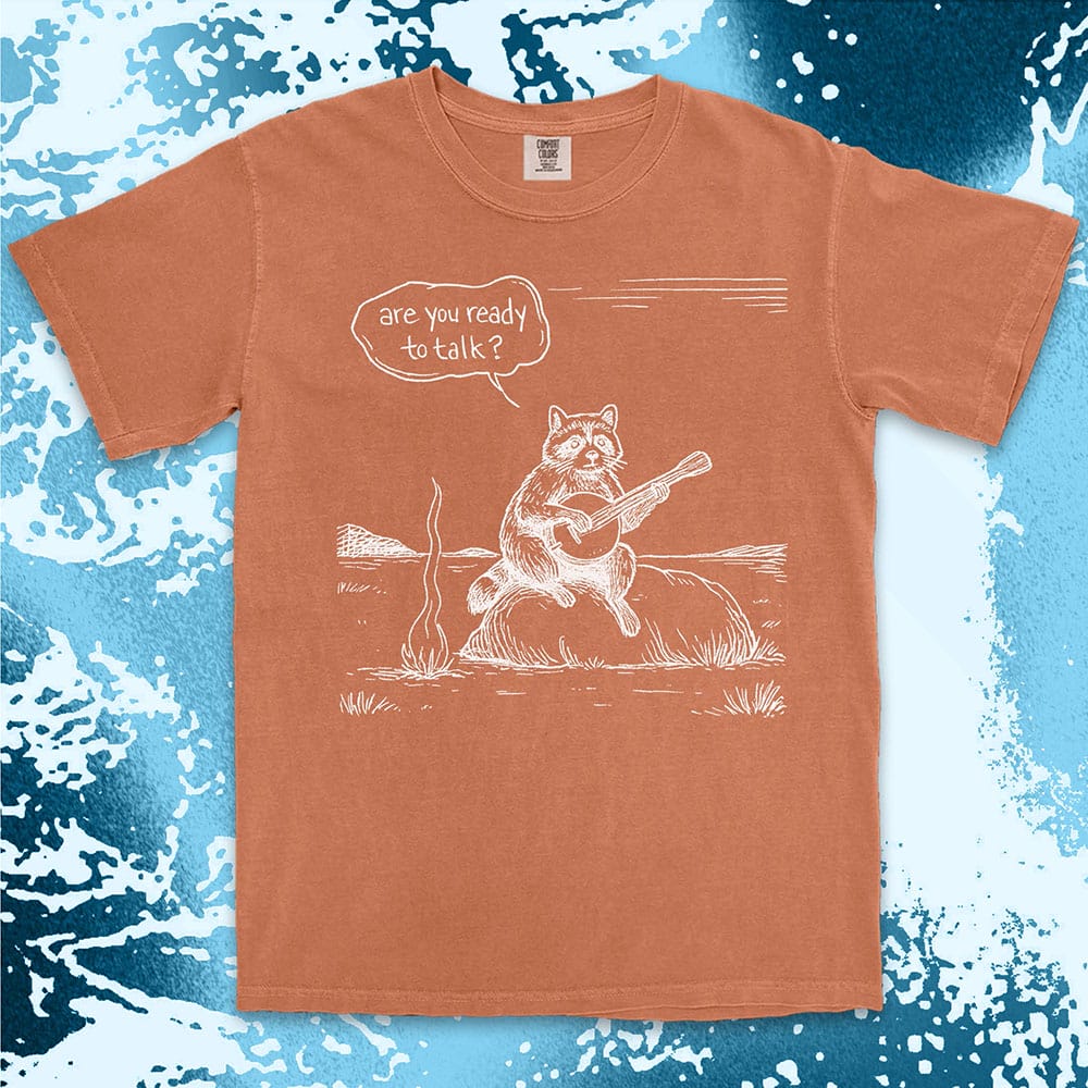 Comfort Color t-shirt with raccoon playing banjo by campfire and speech bubble saying “Are you ready to talk?”
