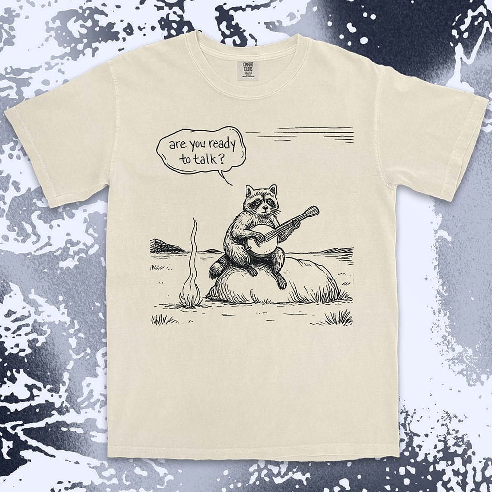 Comfort Color t-shirt with raccoon playing banjo by campfire and speech bubble saying “Are you ready to talk?”