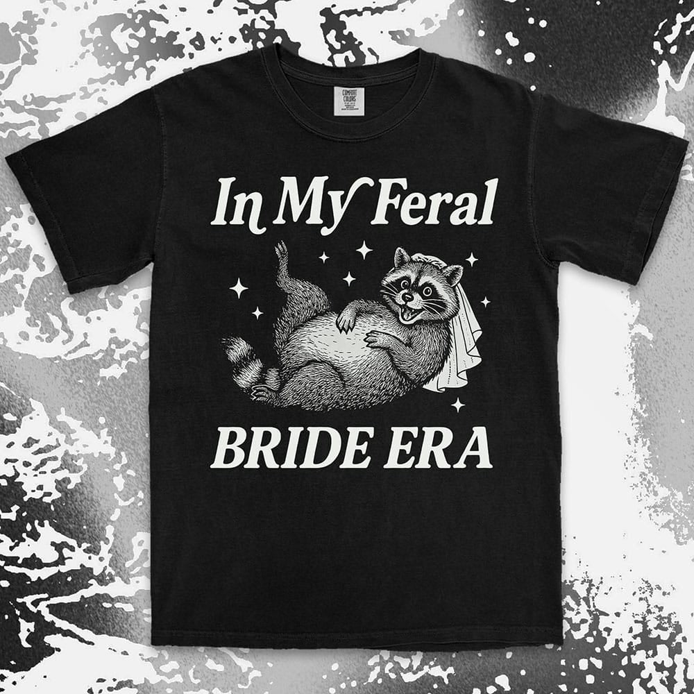 Comfort Color t-shirt with a raccoon wearing a bridal veil and text ÒIn My Feral Bride EraÓ in playful vintage lettering.