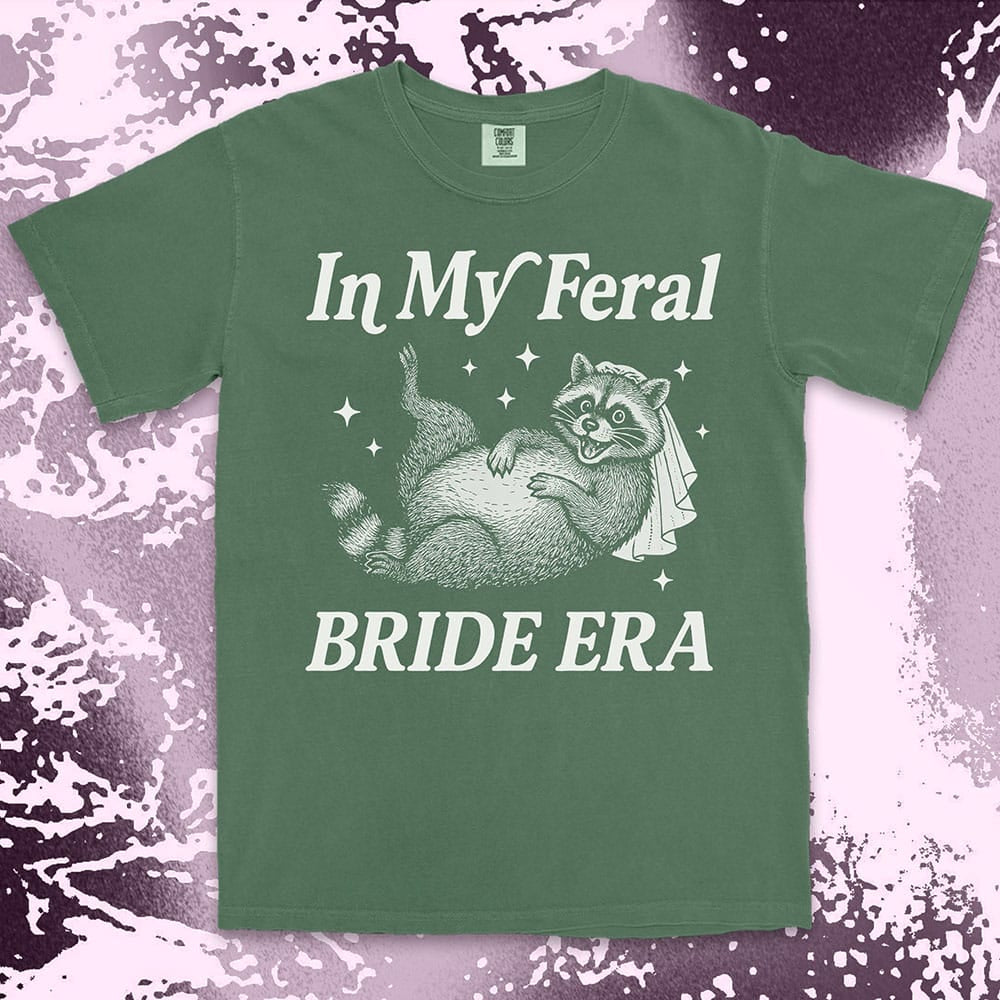 Comfort Color t-shirt with a raccoon wearing a bridal veil and text ÒIn My Feral Bride EraÓ in playful vintage lettering.
