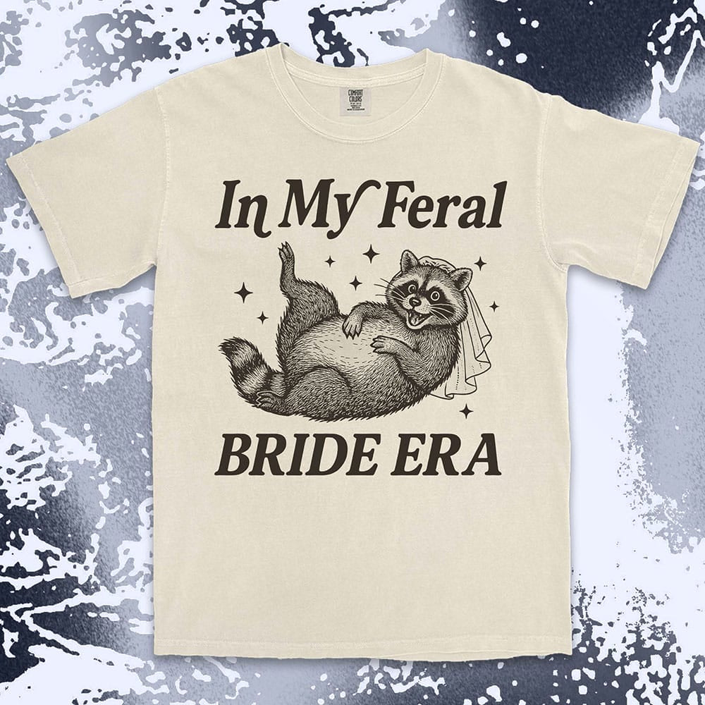 Comfort Color t-shirt with a raccoon wearing a bridal veil and text ÒIn My Feral Bride EraÓ in playful vintage lettering.