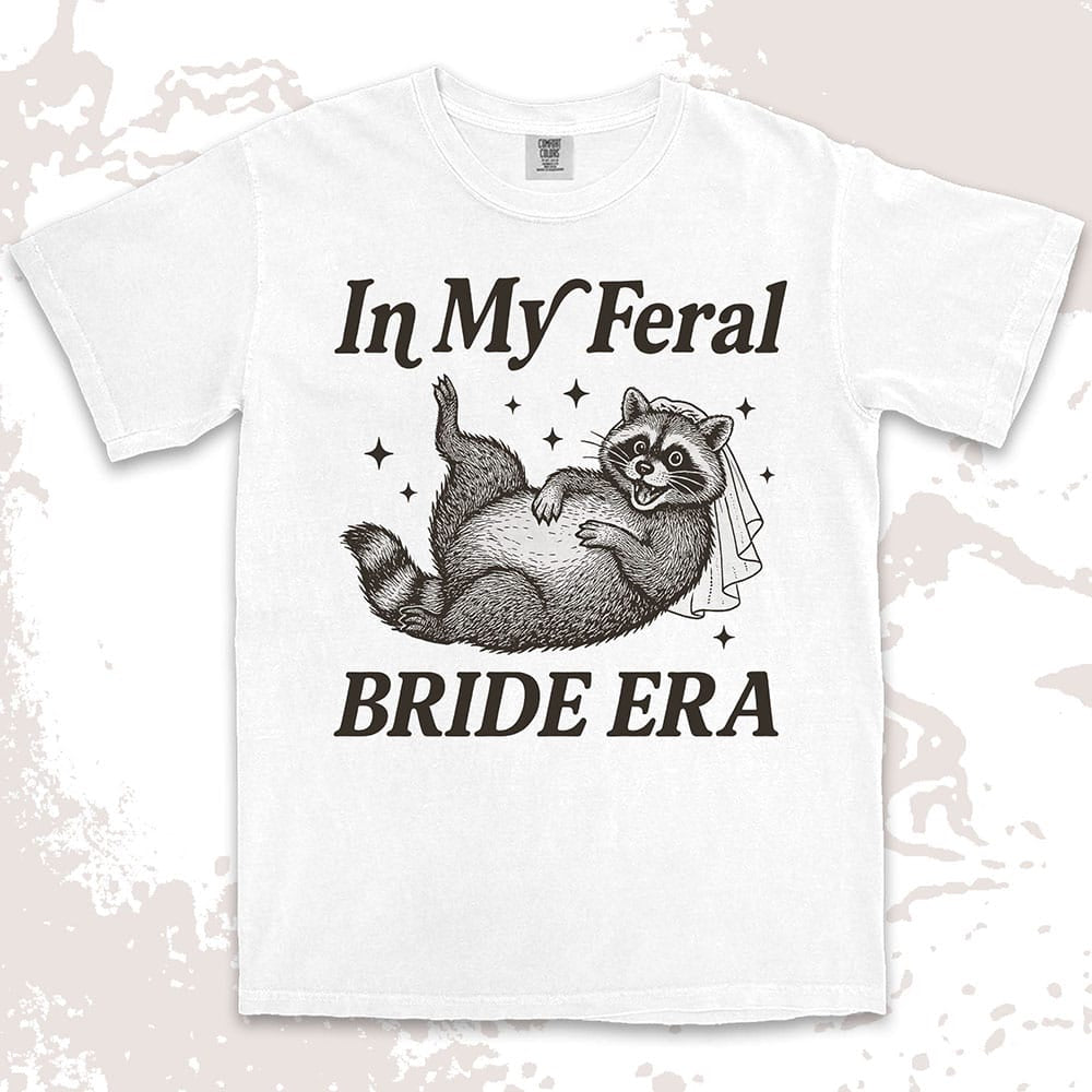 Comfort Color t-shirt with a raccoon wearing a bridal veil and text ÒIn My Feral Bride EraÓ in playful vintage lettering.