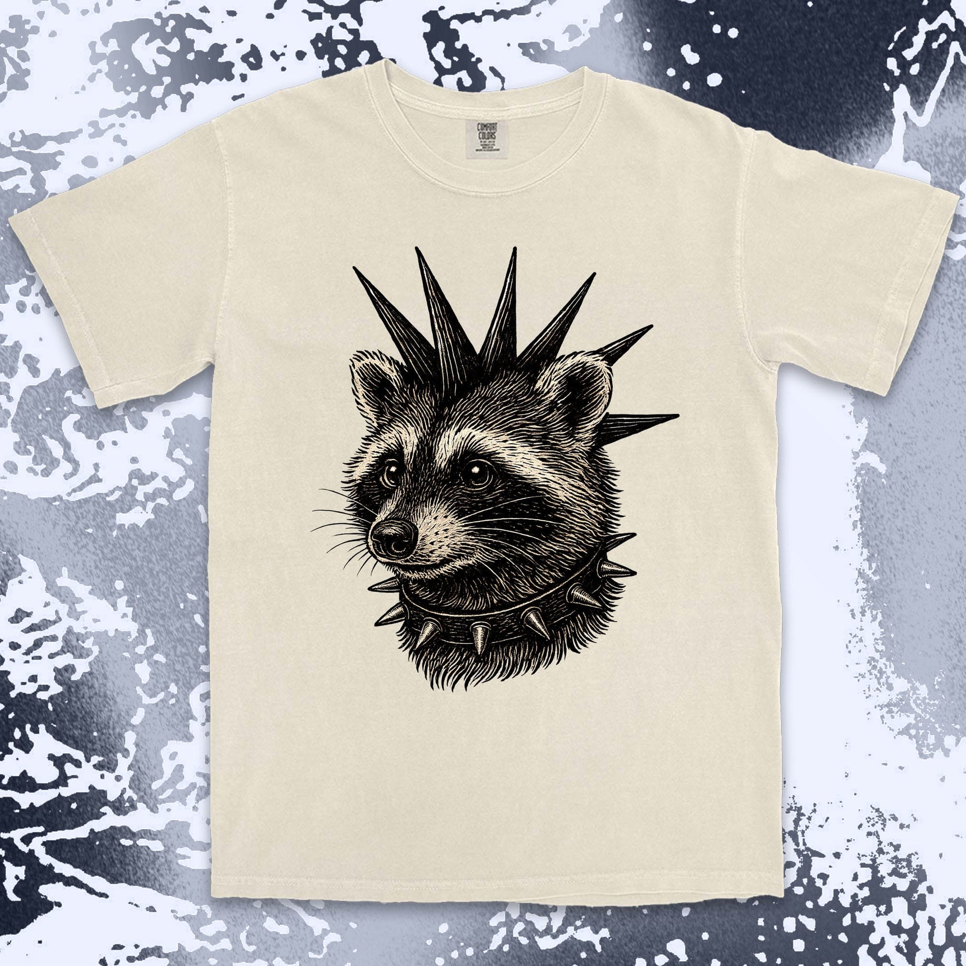 Beige t-shirt with a raccoon design wearing a spiked collar on a textured surface. Ivory color shirt