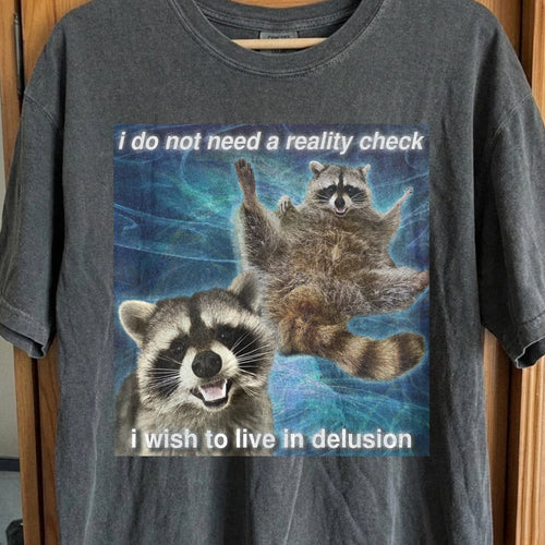 Raccoon t-shirt with quote “I do not need a reality check, I wish to live in delusion” on surreal blue background