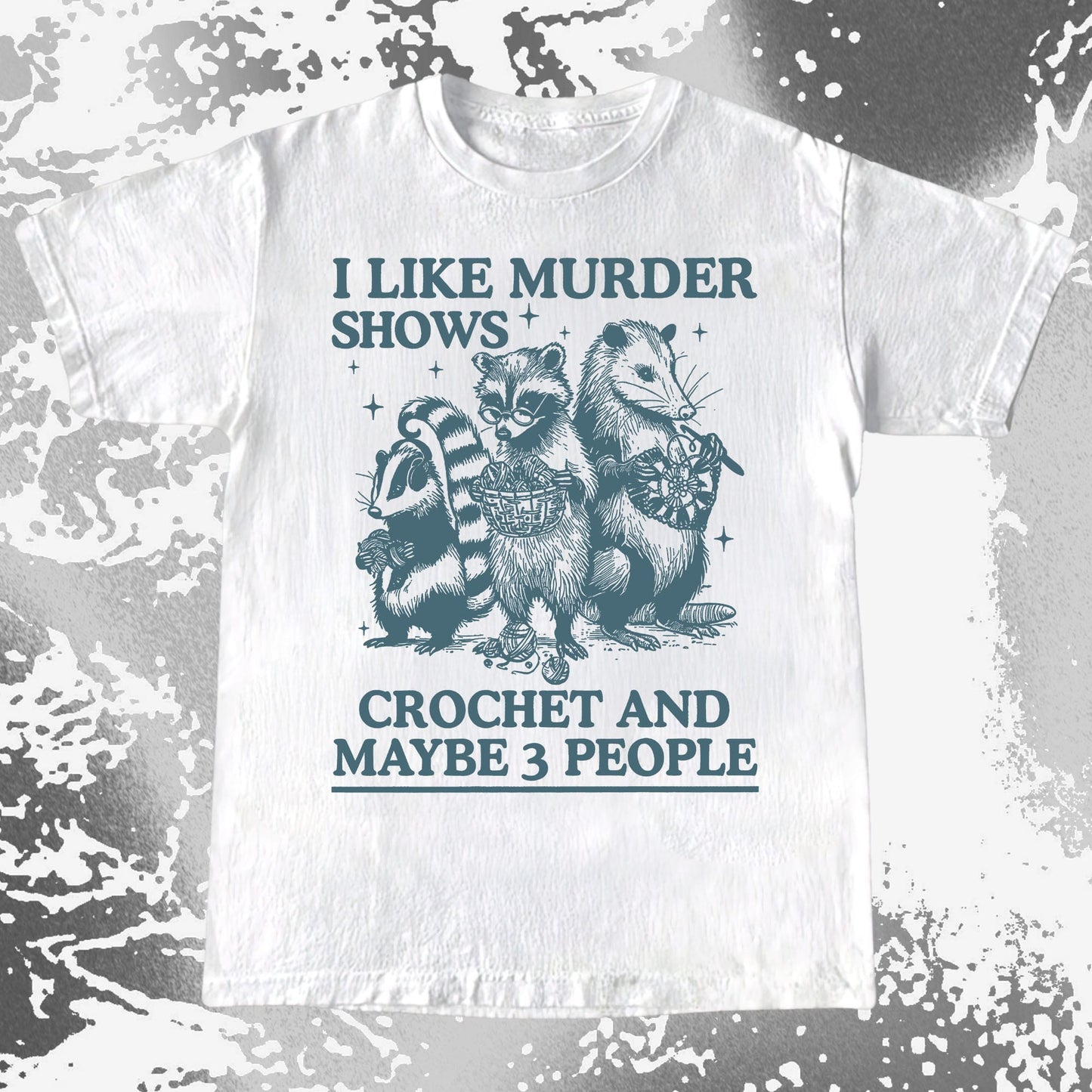 White t-shirt with raccoon graphic and text 'I like murder shows, crochet and maybe 3 people' on a textured background.
