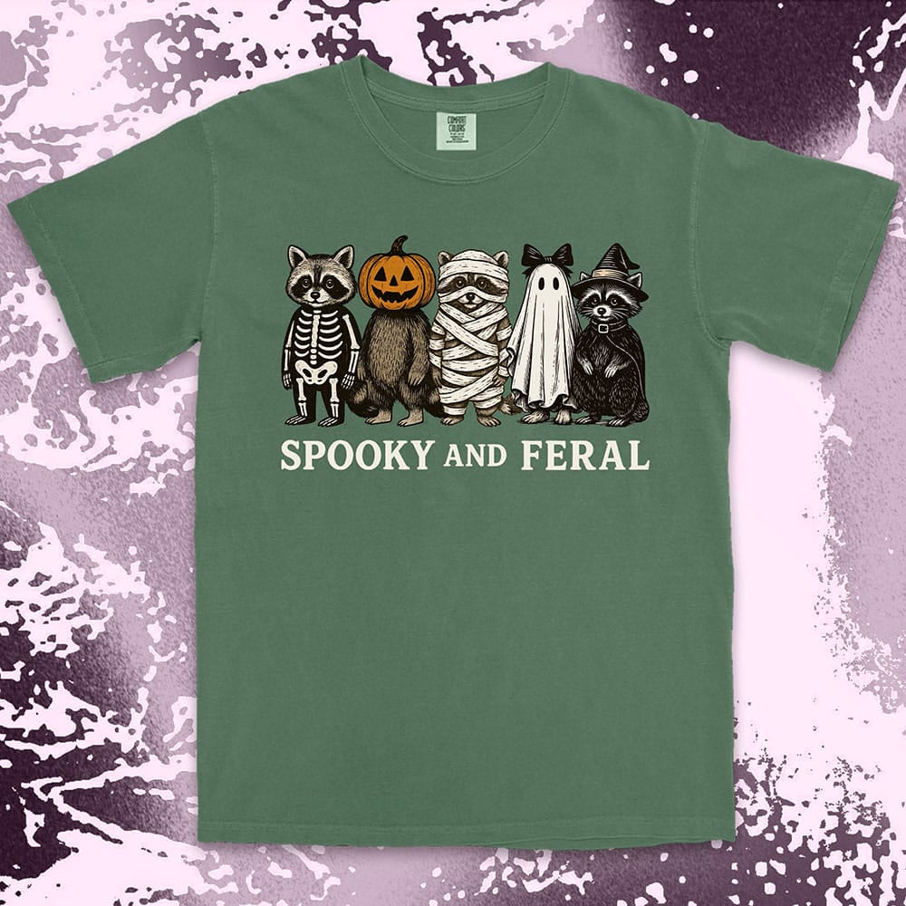 Comfort Color t-shirt with five raccoons in Halloween costumes (skeleton, pumpkin, mummy, ghost, witch) and text “Spooky and Feral.”