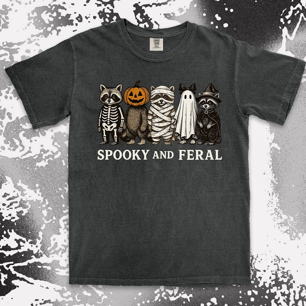 Comfort Color t-shirt with five raccoons in Halloween costumes (skeleton, pumpkin, mummy, ghost, witch) and text “Spooky and Feral.”
