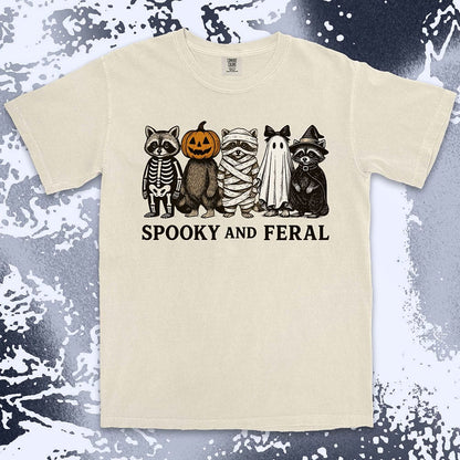 Comfort Color t-shirt with five raccoons in Halloween costumes (skeleton, pumpkin, mummy, ghost, witch) and text “Spooky and Feral.”