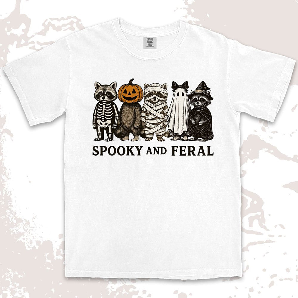 Comfort Color t-shirt with five raccoons in Halloween costumes (skeleton, pumpkin, mummy, ghost, witch) and text “Spooky and Feral.”