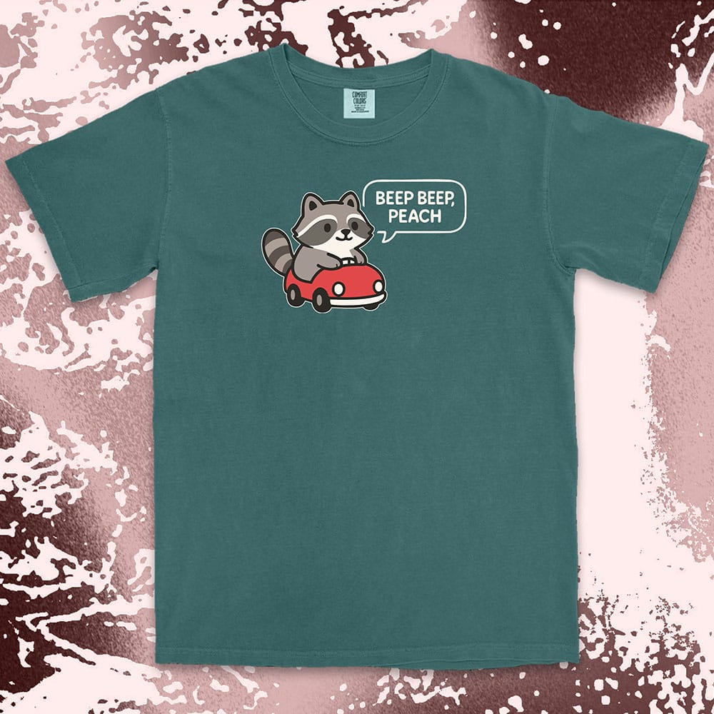 Comfort Color t-shirt with cute chibi raccoon driving a red car and speech bubble saying “Beep beep, peach.”