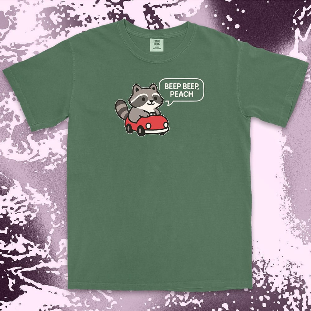 Comfort Color t-shirt with cute chibi raccoon driving a red car and speech bubble saying “Beep beep, peach.”