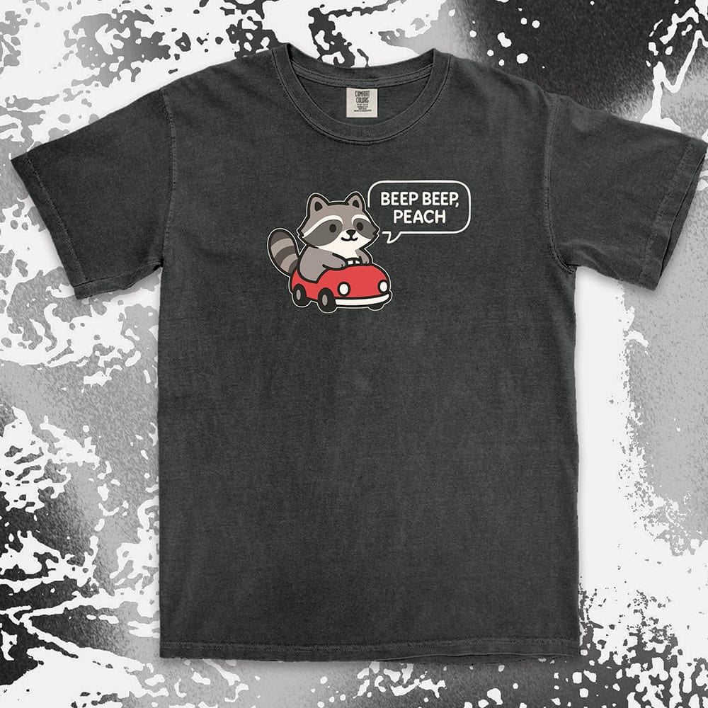 Comfort Color t-shirt with cute chibi raccoon driving a red car and speech bubble saying “Beep beep, peach.”