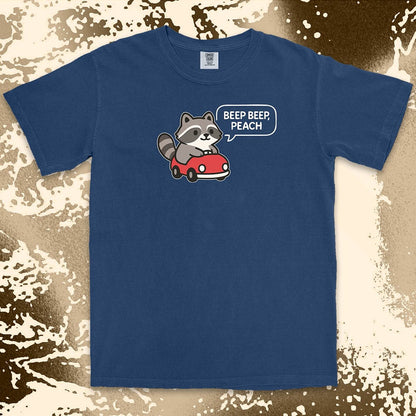Comfort Color t-shirt with cute chibi raccoon driving a red car and speech bubble saying “Beep beep, peach.”
