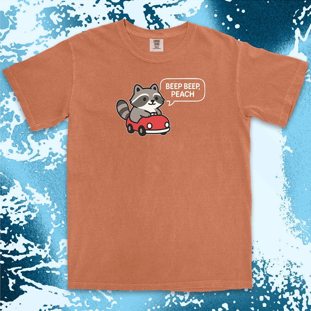 Comfort Color t-shirt with cute chibi raccoon driving a red car and speech bubble saying “Beep beep, peach.”