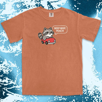 Comfort Color t-shirt with cute chibi raccoon driving a red car and speech bubble saying “Beep beep, peach.”