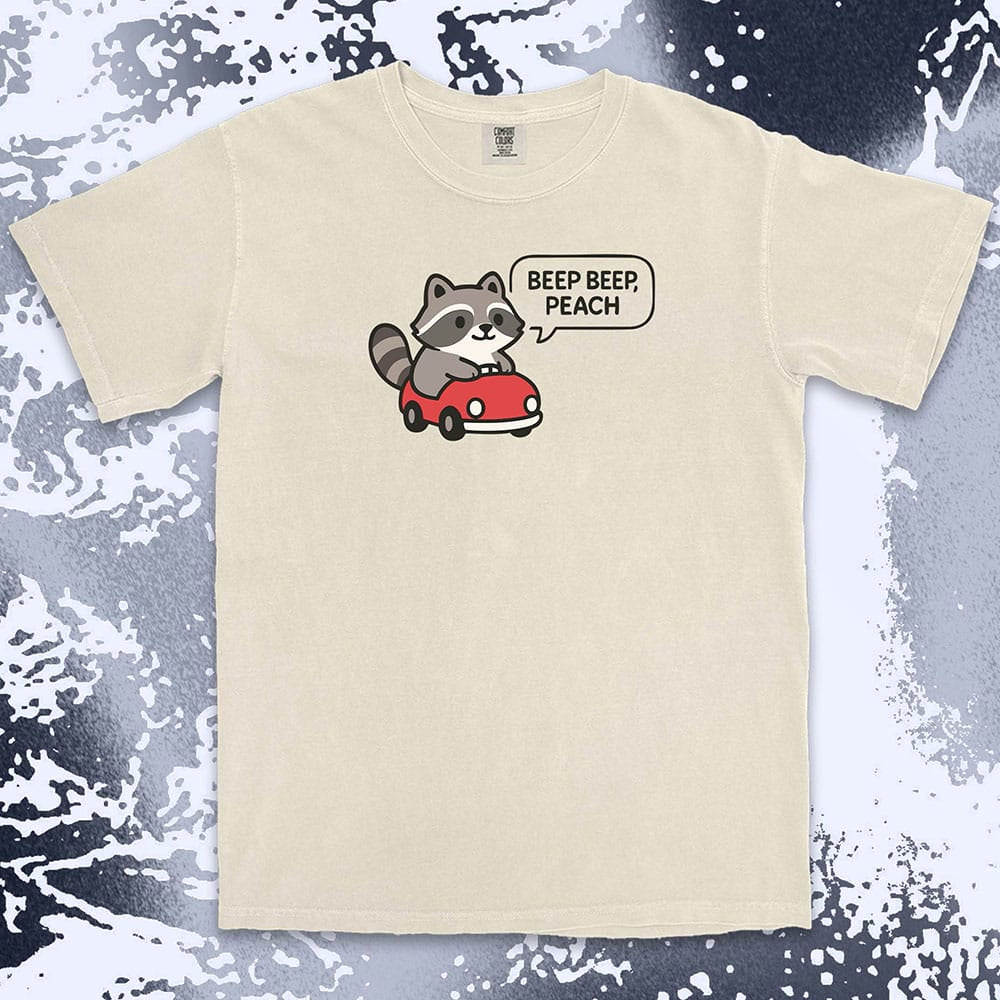 Comfort Color t-shirt with cute chibi raccoon driving a red car and speech bubble saying “Beep beep, peach.”