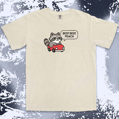 Comfort Color t-shirt with cute chibi raccoon driving a red car and speech bubble saying “Beep beep, peach.”