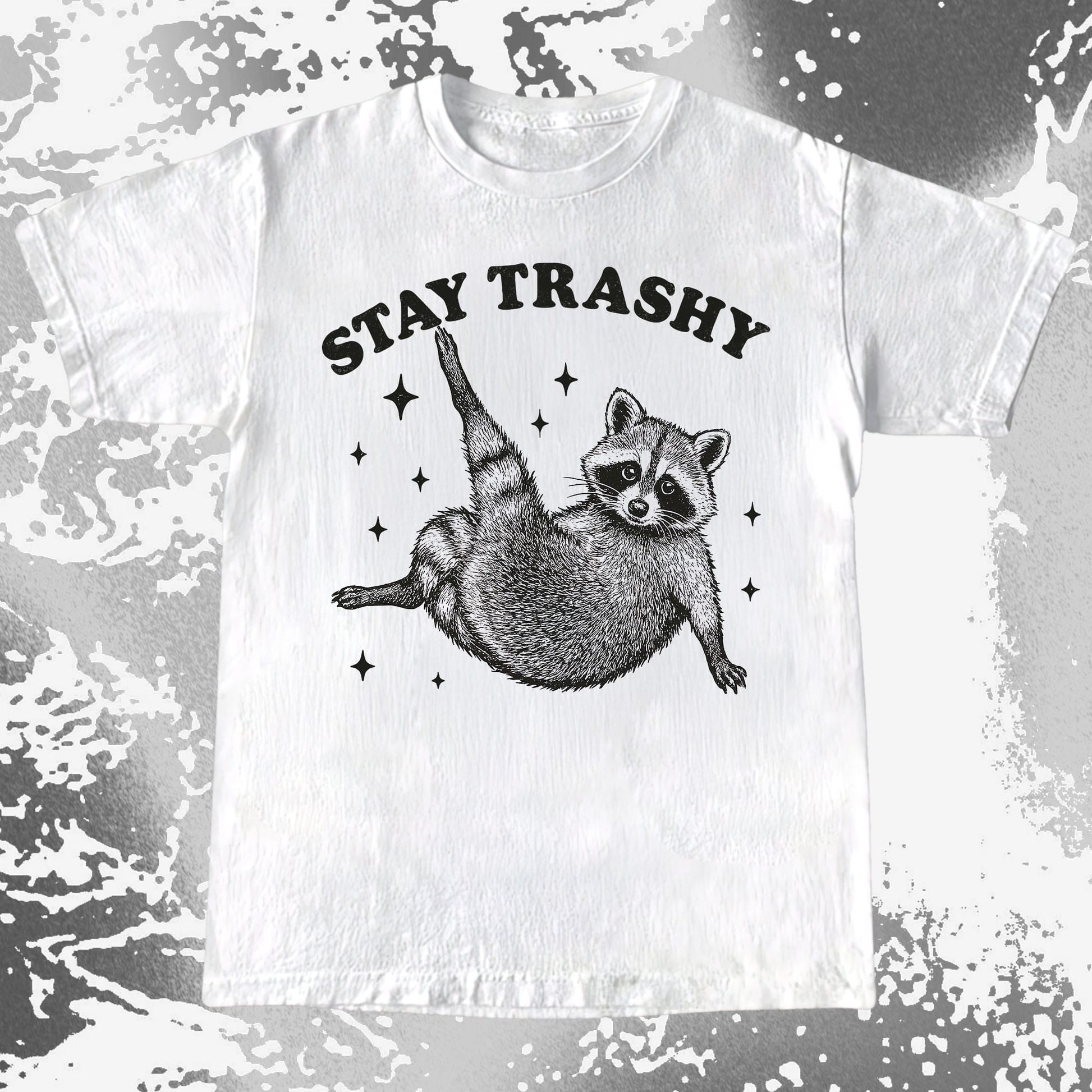 Illustration of a raccoon posing playfully with the text Stay Trashy surrounded by sparkles on a humorous T-shirt design.