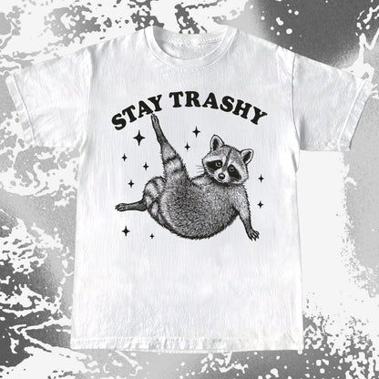Illustration of a raccoon posing playfully with the text Stay Trashy surrounded by sparkles on a humorous T-shirt design.
