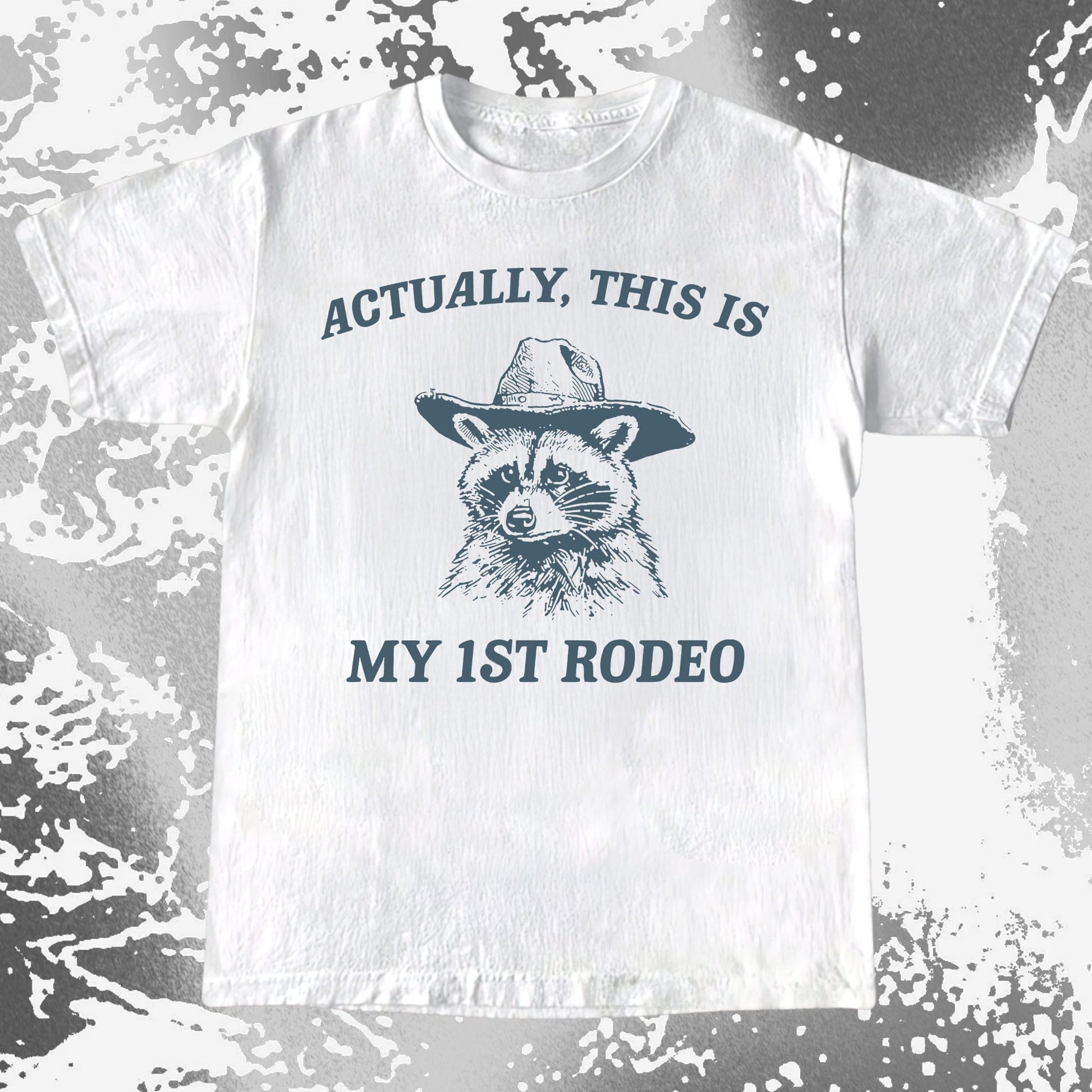 Raccoon wearing a cowboy hat with the text Actually This Is My 1st Rodeo on a humorous T-shirt design.