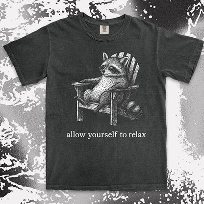 Comfort Color t-shirt with raccoon lounging on a chair and text “Allow yourself to relax” in a calm design.