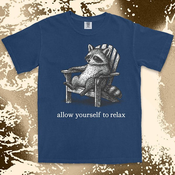 Comfort Color t-shirt with raccoon lounging on a chair and text “Allow yourself to relax” in a calm design.