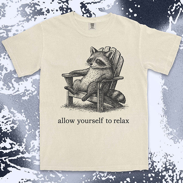 Comfort Color t-shirt with raccoon lounging on a chair and text “Allow yourself to relax” in a calm design.