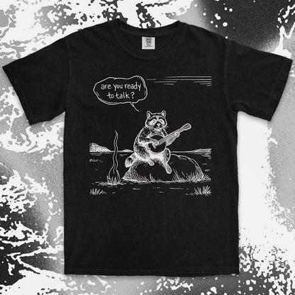 Comfort Color t-shirt with raccoon playing banjo by campfire and speech bubble saying “Are you ready to talk?”