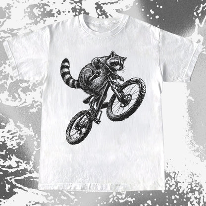 White t-shirt with a black and white illustration of a raccoon riding a bicycle on a distressed background.