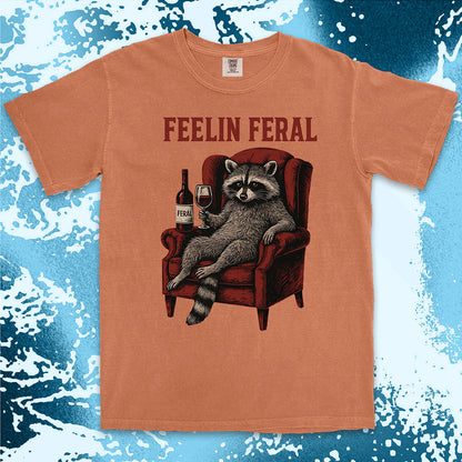 Orange t-shirt with a raccoon graphic and 'FEELIN FERAL' text on a blue and white abstract background