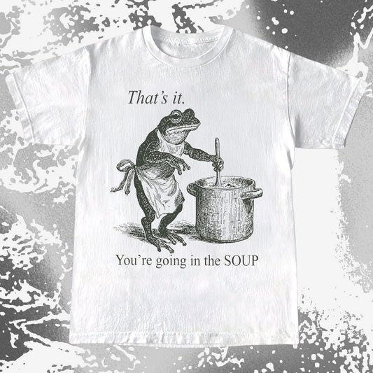 White t-shirt with a graphic of a frog cooking in a pot and text 'That's it. You're going in the SOUP' on a textured background.