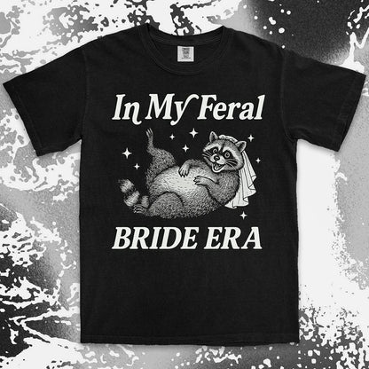 Comfort Color t-shirt with a raccoon wearing a bridal veil and text ÒIn My Feral Bride EraÓ in playful vintage lettering.