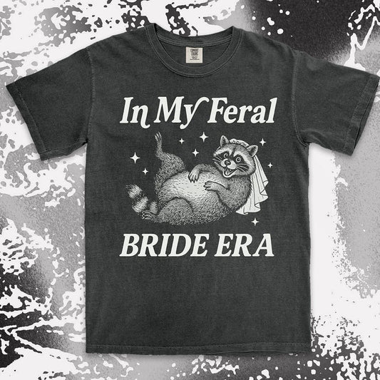 Comfort Color t-shirt with a raccoon wearing a bridal veil and text ÒIn My Feral Bride EraÓ in playful vintage lettering.