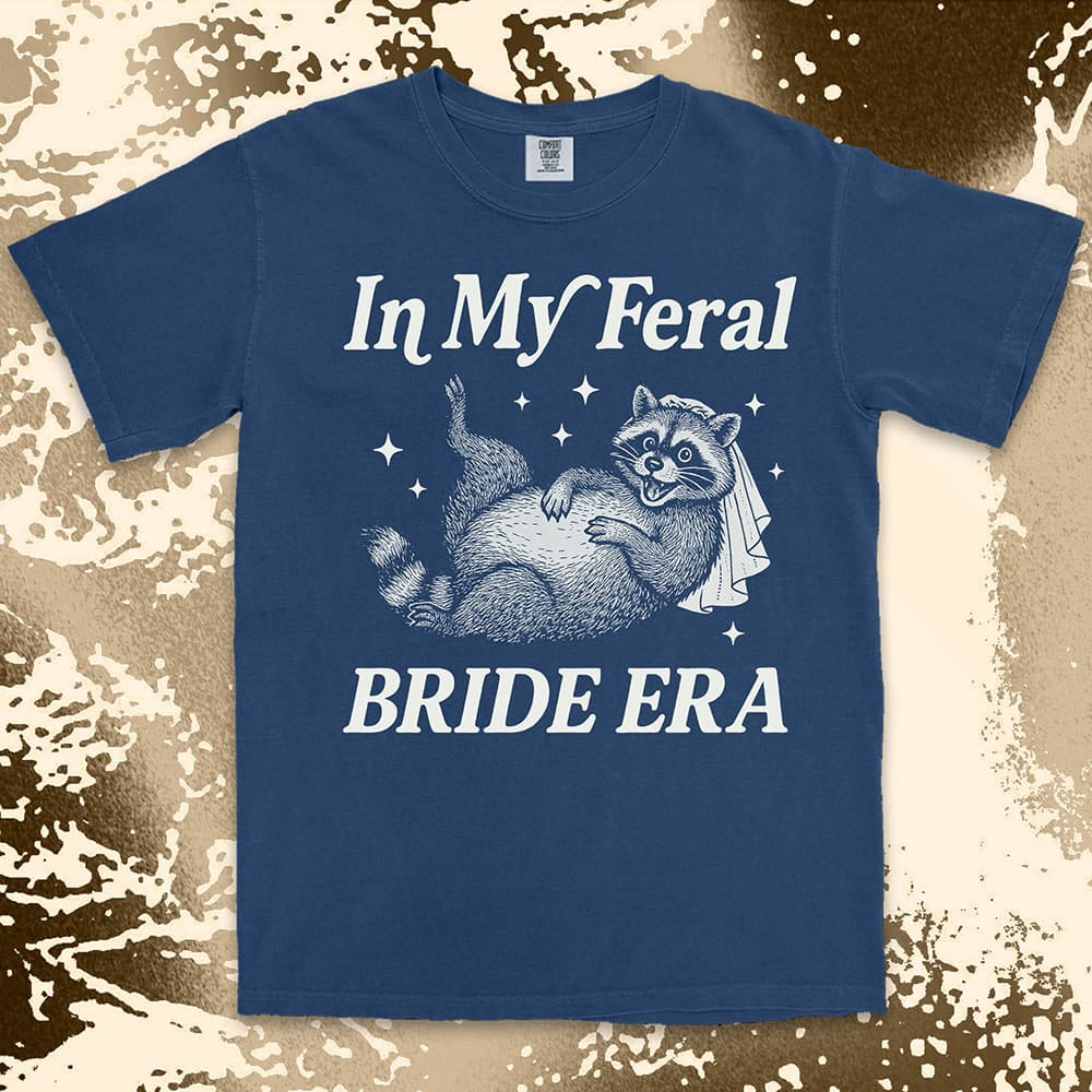 Comfort Color t-shirt with a raccoon wearing a bridal veil and text ÒIn My Feral Bride EraÓ in playful vintage lettering.