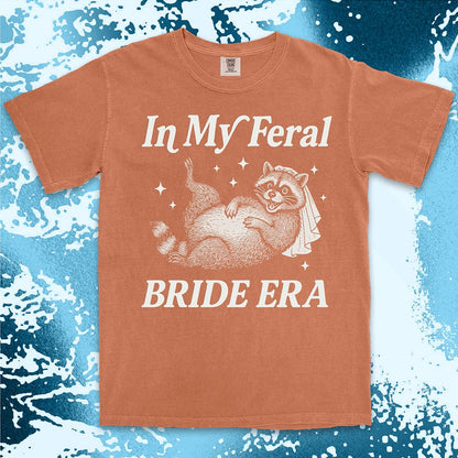 Comfort Color t-shirt with a raccoon wearing a bridal veil and text ÒIn My Feral Bride EraÓ in playful vintage lettering.
