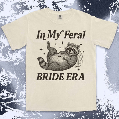 Comfort Color t-shirt with a raccoon wearing a bridal veil and text ÒIn My Feral Bride EraÓ in playful vintage lettering.