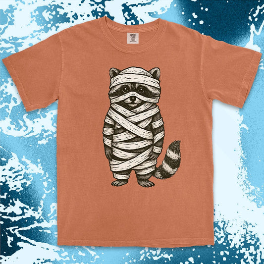 Comfort Color t-shirt with raccoon dressed as a mummy wrapped in bandages for Halloween.