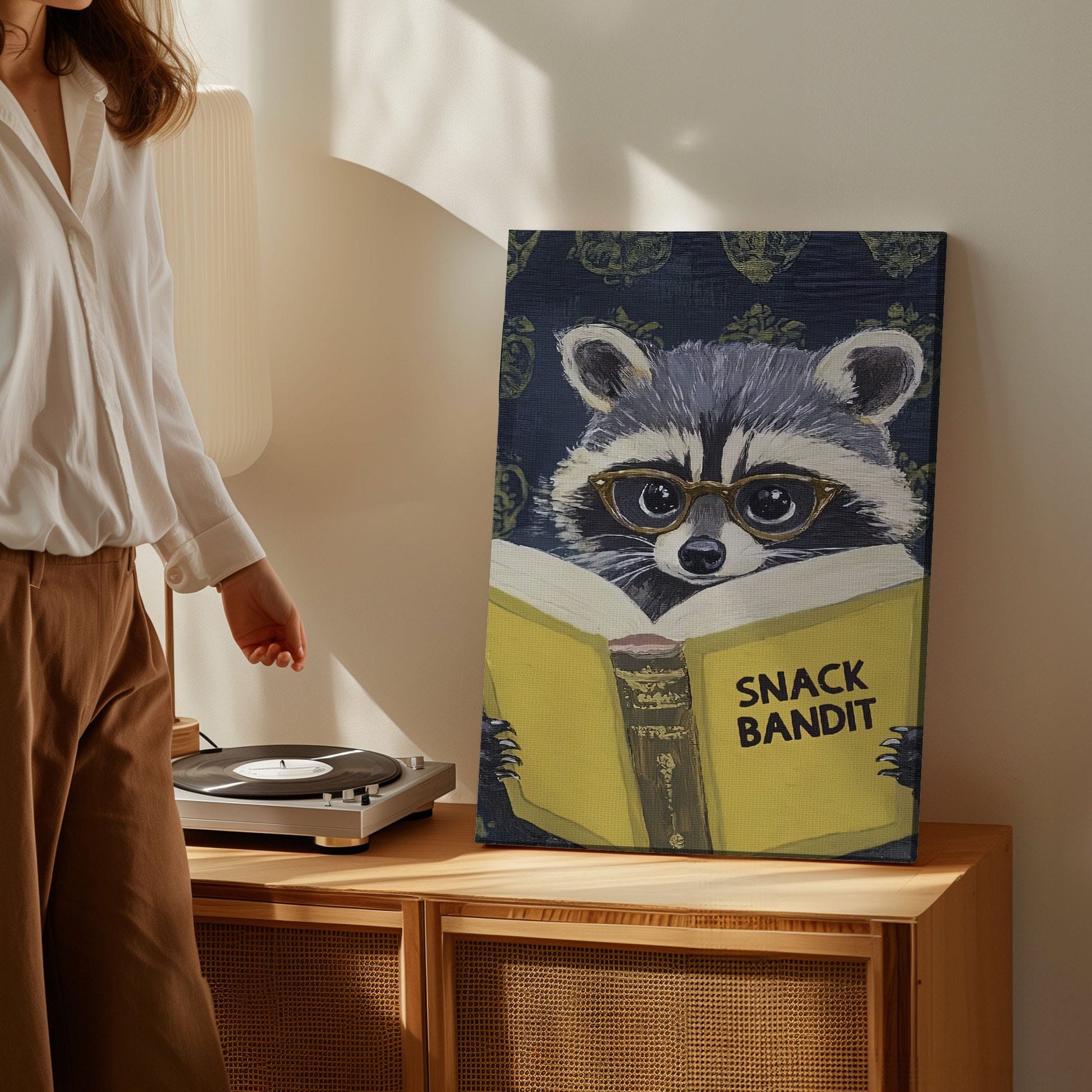 Snack Bandit raccoon canvas wall art featuring a raccoon wearing glasses reading a yellow book in vintage playful style