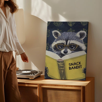 Snack Bandit raccoon canvas wall art featuring a raccoon wearing glasses reading a yellow book in vintage playful style