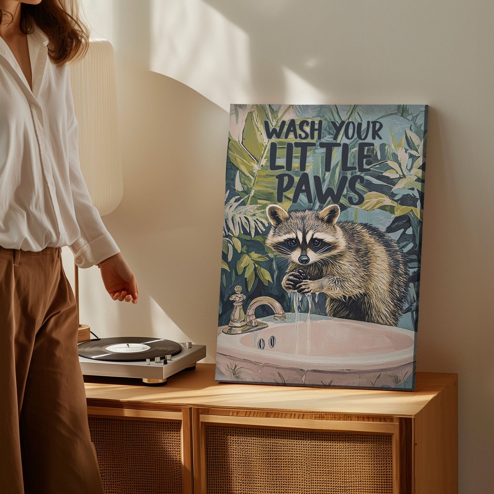 Wash Your Little Paws raccoon canvas wall art featuring a raccoon washing hands at sink with green tropical leaves background