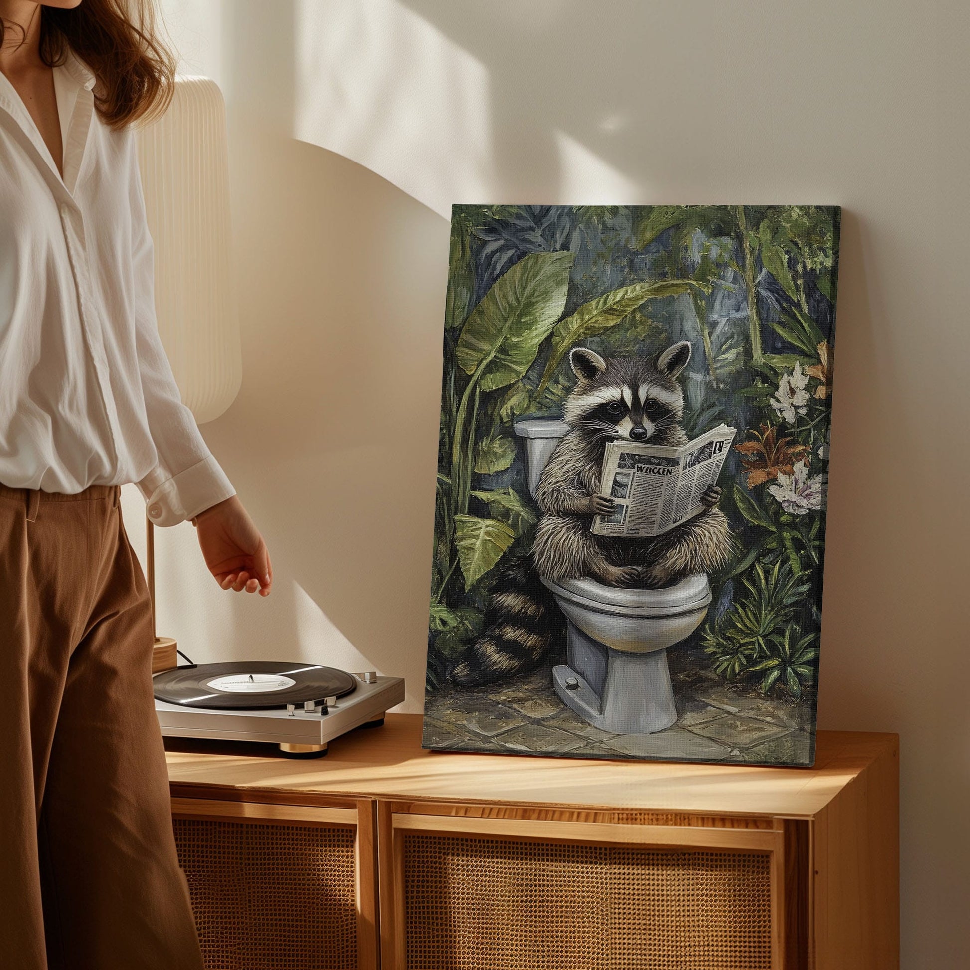 Bathroom raccoon canvas wall art featuring a raccoon sitting on toilet reading a newspaper surrounded by green tropical plants